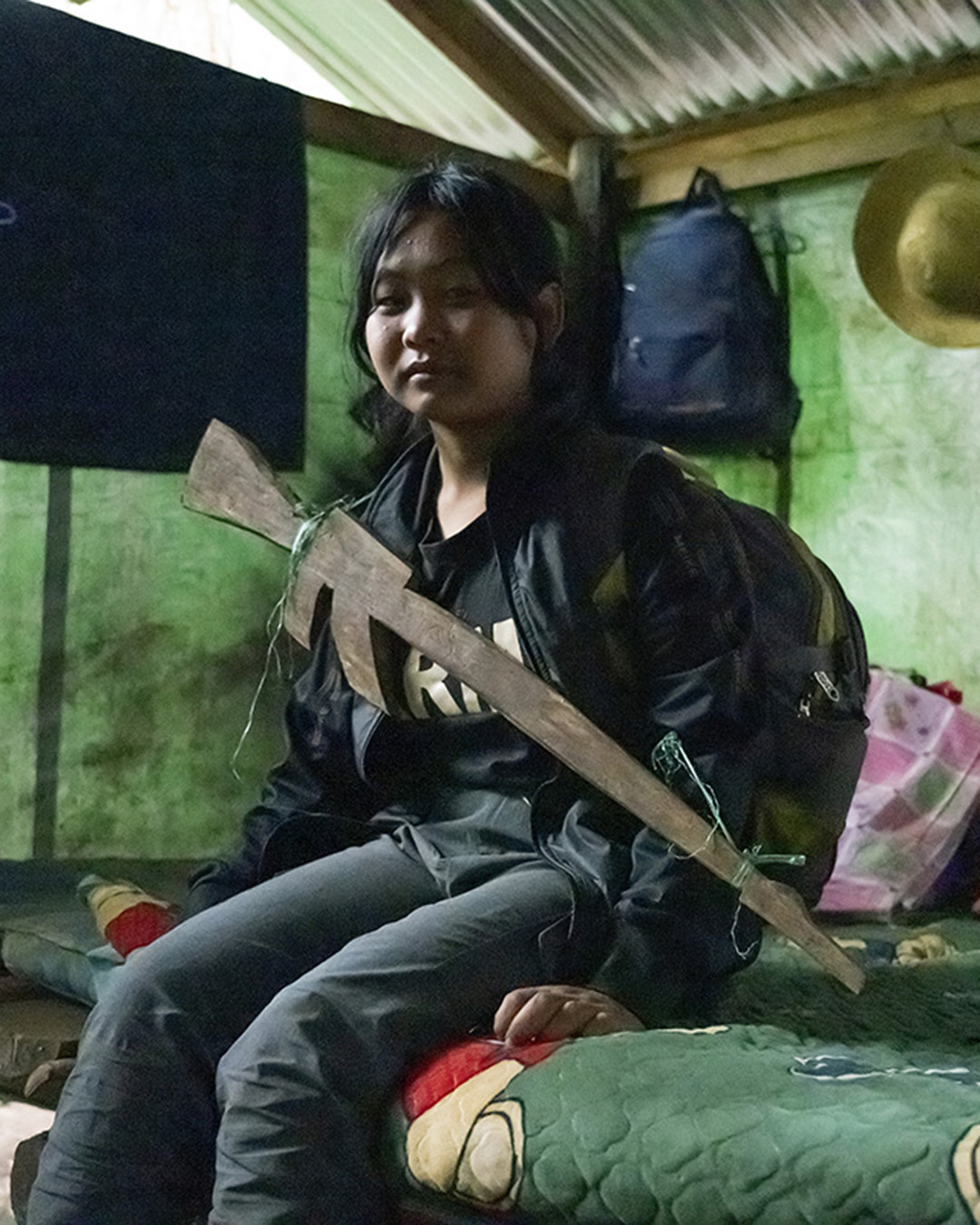 Young woman sits on bed with a fake wooden rifle around her neck