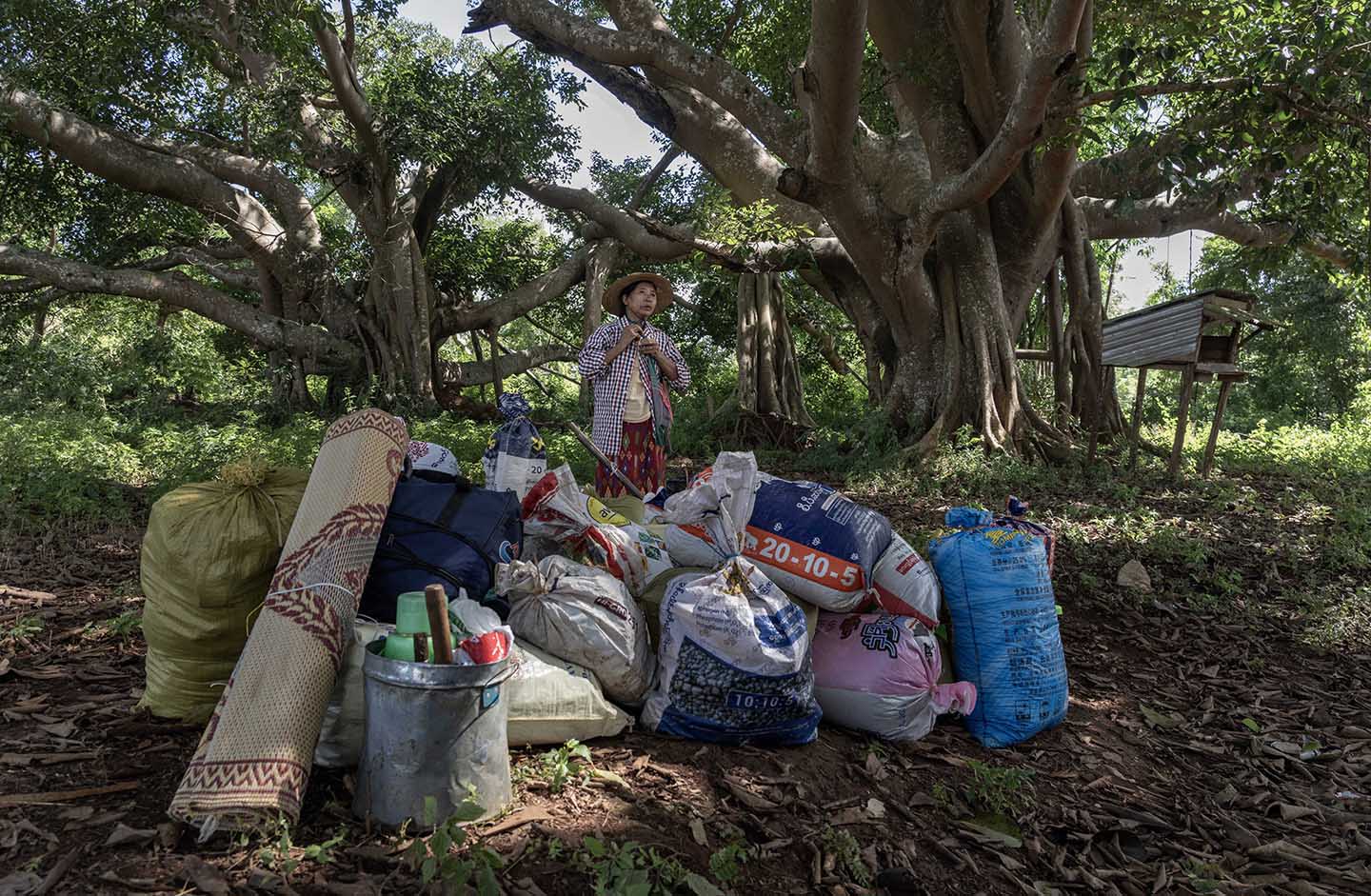 A woman with a pile of rice bags waits by a large tree