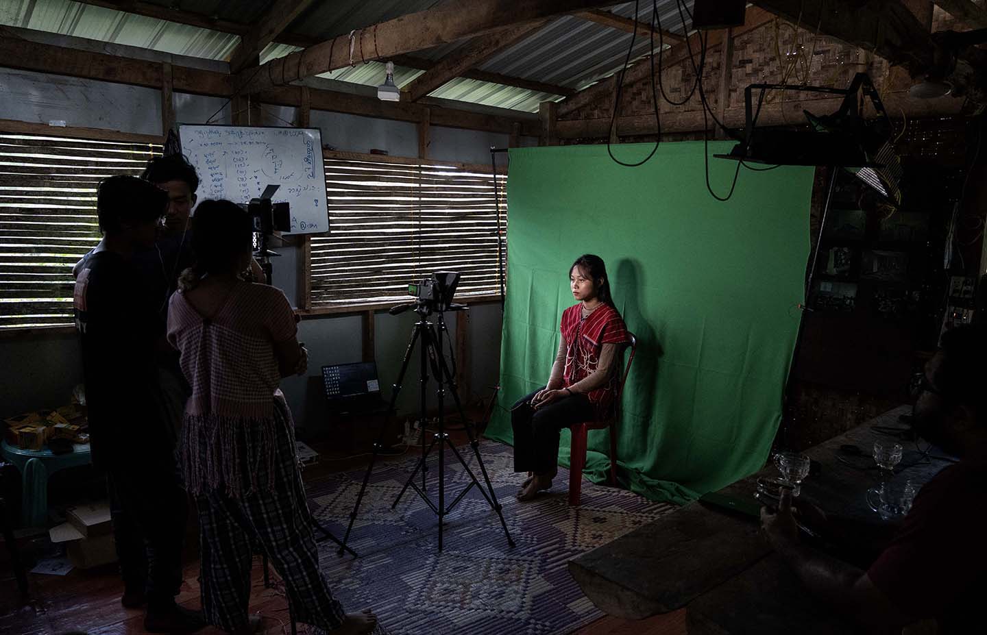 A woman sits in front of a green screen, cameras trained on her