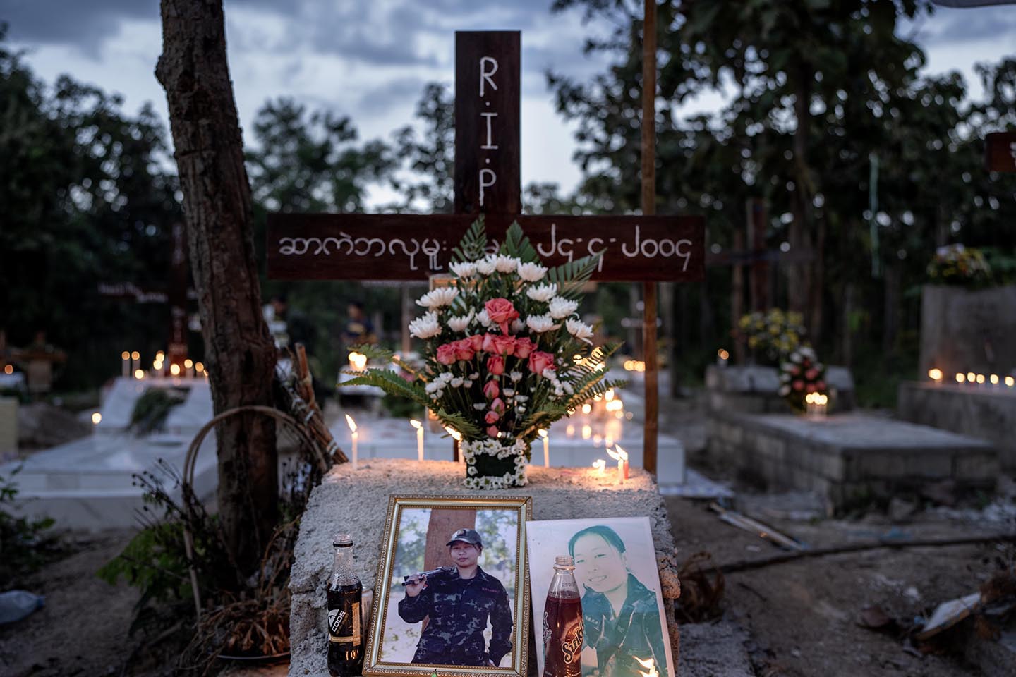 A cross stands behind a stone marker and framed photographs at a grave