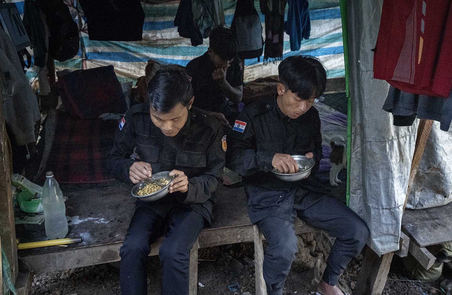 Two officers sit on a bench and eat from bowls