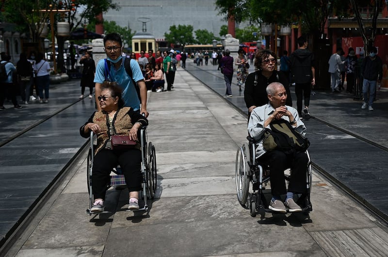 2021年5月11日，在北京的一条街道上，一对老年男女被推着坐在轮椅上。 （法新社）