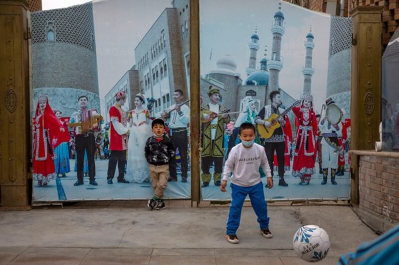 Children play soccer in front of a gate with a mural depicting Uyghur musicians in Urumqi, capital of northwest China's Xinjiang region, April 21, 2021, during a government organized trip for foreign journalists. (Mark Schiefelbein/AP)