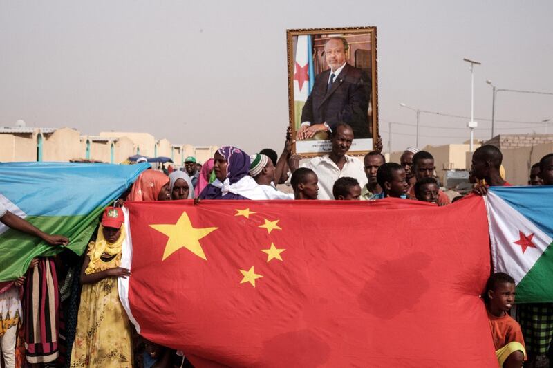 People hold Chinese and Djiboutian national flags with the portrait of Djibouti's President Ismail Omar Guellehas as they wait for the arrival of the president before the launching ceremony of new Chinese-funded 1000-unit housing construction project in Djibouti, July 4, 2018. Credit: AFP