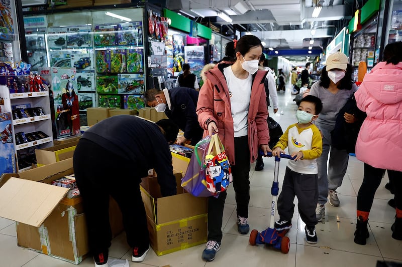 A woman and a child walk past workers sorting toys at a shopping mall in Beijing, Jan. 11, 2023. (Tingshu Wang/Reuters)