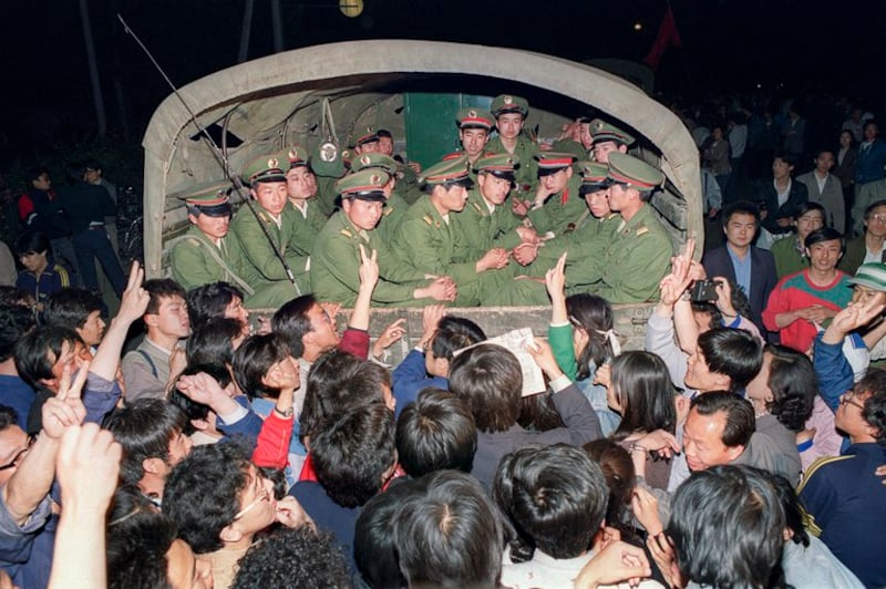 1989年5月20日，民主示威民众举起拳头、做出胜利的手势，拦下一辆载有士兵的军用卡车，阻挡其驶向天安门广场。（亨丽埃特/法新社）