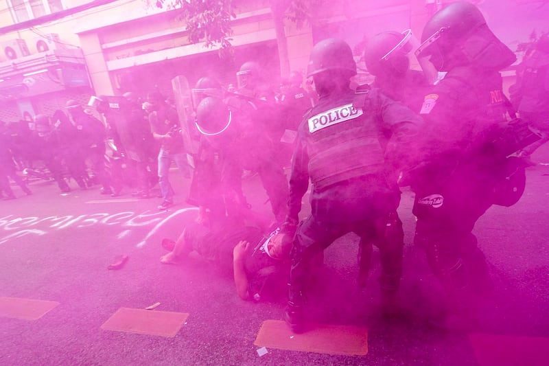 In cloud of pink smoke, police in riot gear remove a protester trying to march to the Asia-Pacific Economic Cooperation APEC summit venue, Nov. 18, 2022, in Bangkok, Thailand. (Wason Wanichakorn/AP)