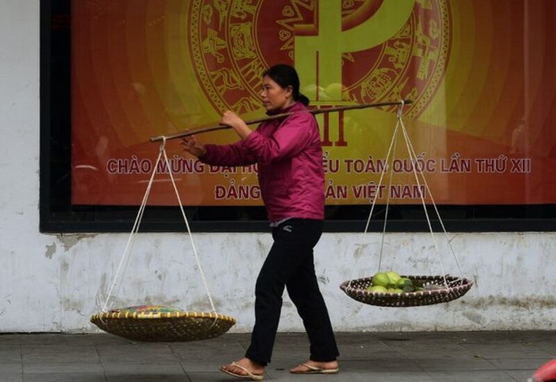 Một phụ nữ gánh hàng rong đi qua một pano tuyên truyền Đại hội đảng toàn quốc trên đường phố Hà Nội ngày 15/01/16.