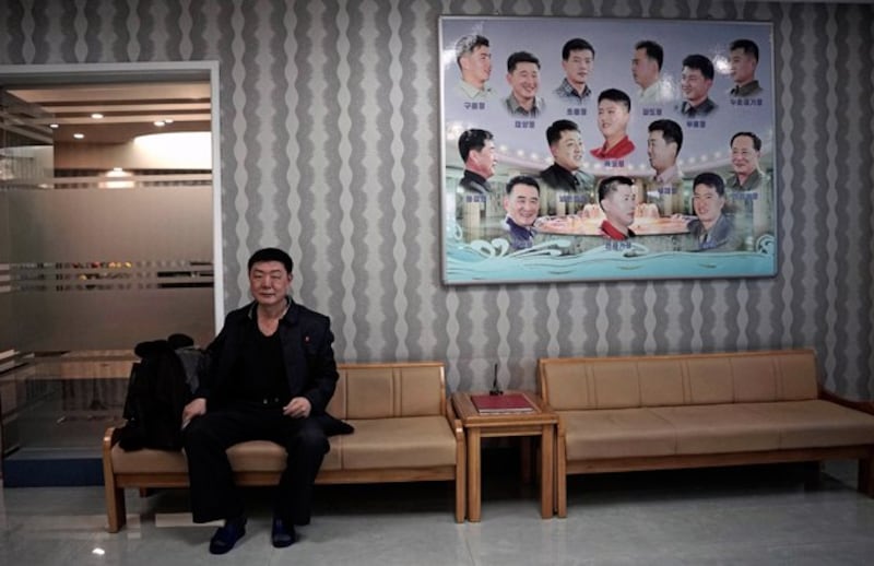 A North Korean man waits outside a barber shop next to a poster with different types of hairstyles in Pyongyang in 2015. Credit: Wong Maye-E/AP