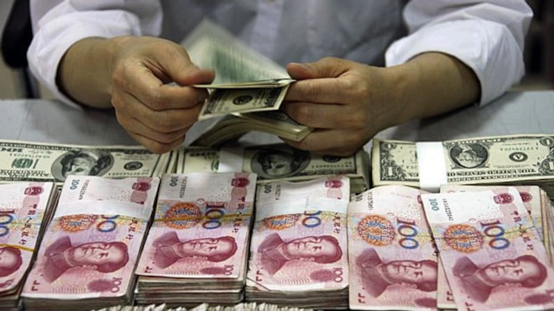 A Chinese bank teller counts US dollar notes next to stacks of Chinese 100 yuan at a bank in Huaibei, eastern China's Anhui province, Sept. 24, 2013.