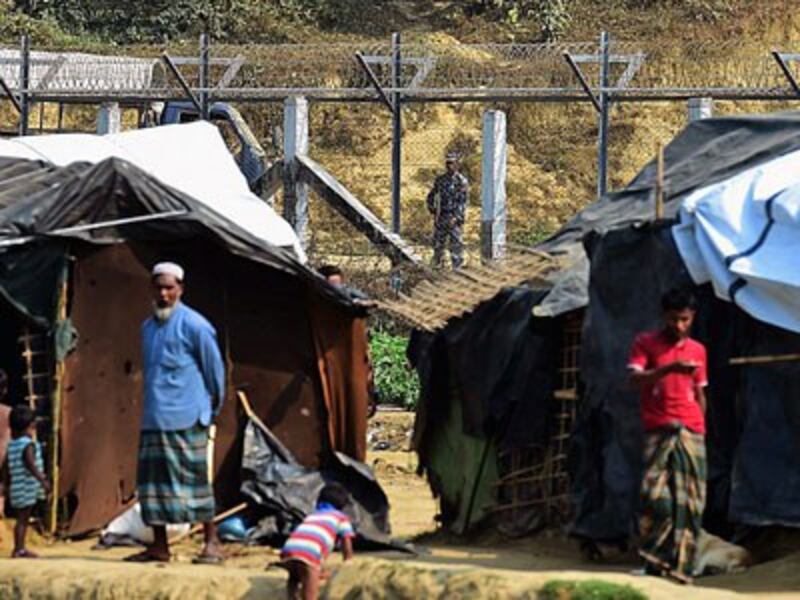 A Myanmar security guard keeps watch along the Myanmar-Bangladesh border as Rohingya refugees stand outside their makeshift shelters near Tombru in southeastern Bangladesh's Bandarban district, March 1, 2018.