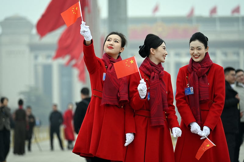 Attendants hold Chinese flags in Tiananmen Square following the closing session of the National People's Congress  in Beijing, March 11, 2025.