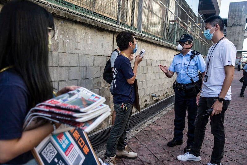 In this Aug. 11, 2020 photo, security officers ask pro-democracy district councilor Ng Kin-wai to not to use a megaphone while volunteers hand out free copies of the Apple Daily newspaper in Hong Kong. Credit: AP