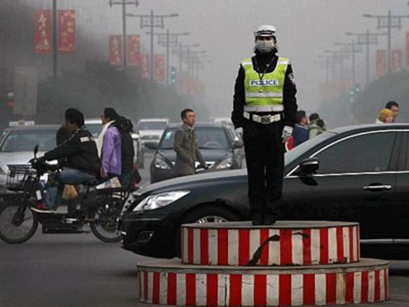 A traffic police officer wearing a face mask directs vehicles on a road in heavy smog in Xi'an, northern China's Shaanxi province, Feb. 2, 2014.