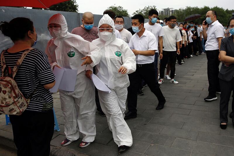 2020年6月17日，北京爆发第二波新冠病毒疫情后，穿着防护服的医务人员在排队等候人员进行核酸检测。（路透社）