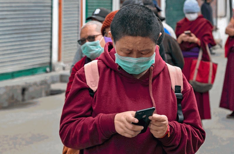 An exile Tibetan Buddhist nun uses her mobile phone as she waits with others in a line to receive free rations distributed by a Tibetan Buddhist monk during a lockdown to curb the spread of the coronavirus in Dharmsala, India, April 28, 2020. Credit: Associated Press