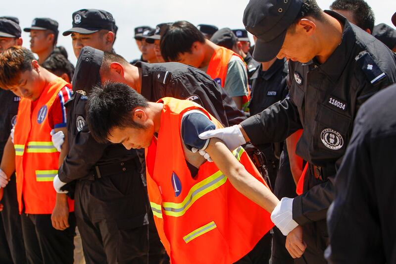 Chinese, in orange vest, arrested over an alleged internet scam, are escorted by Chinese police officers before boarding at Phnom Penh International Airport, in Phnom Penh, Cambodia, Thursday, Oct. 12, 2017. (Heng Sinith/AP)