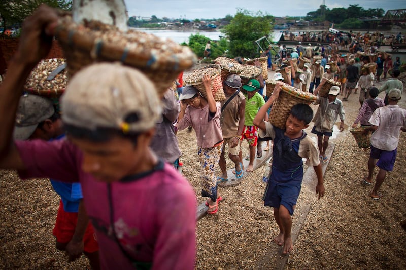 A child, right, carries a basket of stones while unloading a quarry boat with adult workers at a port in Yangon, Myanmar, Sept. 2, 2012. (Alexander F. Yuan/AP)