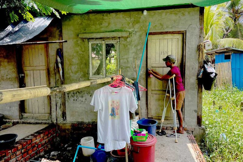 Ko Phyo uses his crutches to balance as he locks his home. He's been learning to use his crutches when outdoors to deal with the uneven roads and paths that run between the fields of his township. (REUTERS)