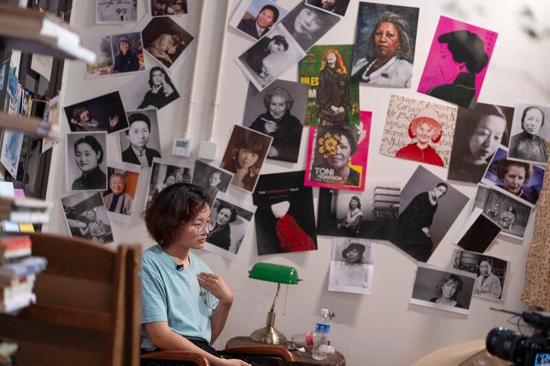 Lu Sirui sits near a wall covered with photos of female personalities at a bookstore specializing in feminist literature in Beijing on Thursday, July 27, 2023. (Ng Han Guan/AP)