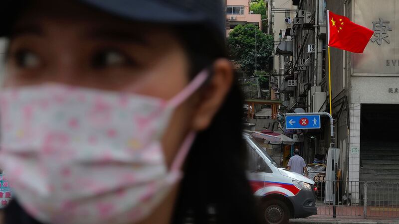 2021 年 7 月 1 日，在香港的一条街道上，一名妇女走过一辆停在中国国旗下的警车。 （美联社）