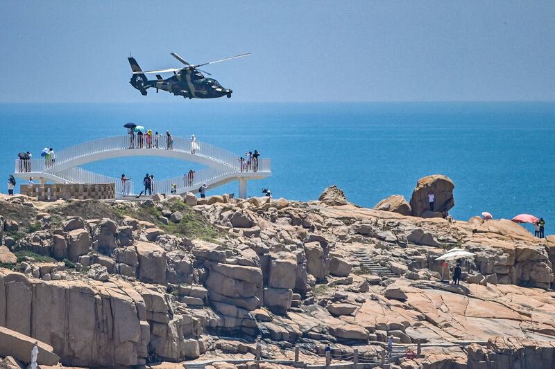 Tourists look on as a Chinese military helicopter flies past Pingtan island, one of mainland China's closest points to Taiwan, in Fujian province on August 4, 2022. Credit: AFP