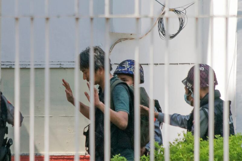 Japanese journalist Yuki Kitazumi raises his hands as he is escorted by police upon arrival at the Myaynigone police station in Sanchaung township in Yangon, Feb. 26, 2021. Credit: AP Photo