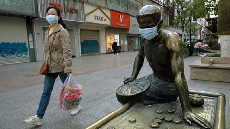 A woman passes a bronze statue covered with a face mask on a partially closed retail street in Wuhan, central China's Hubei province, April 13, 2020. 