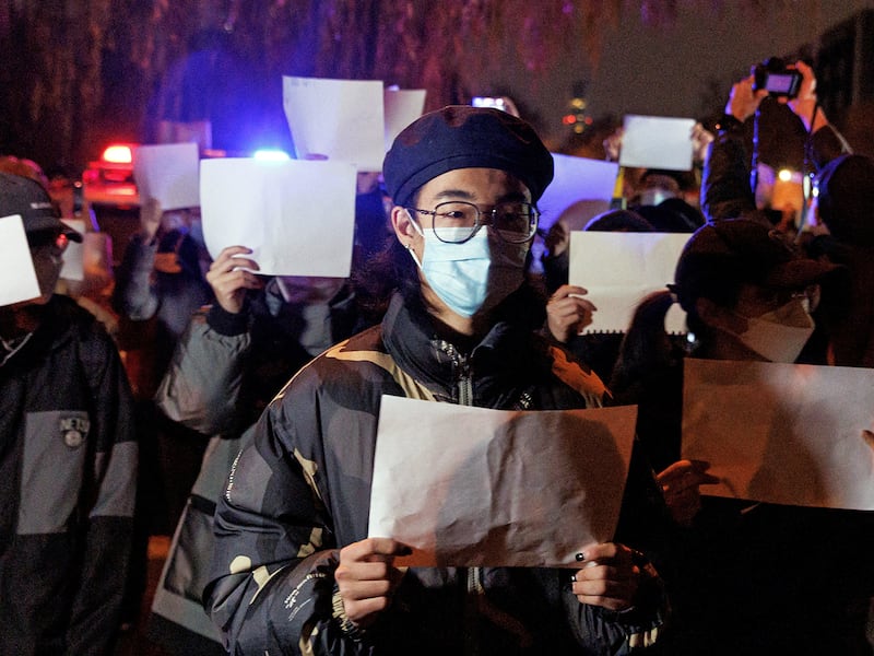 People gather for a vigil and hold white sheets of paper in protest, in Beijing, over coronavirus disease restrictions, during a commemoration of the victims of a fire in Urumqi, China, Nov. 27, 2022. (Reuters/Thomas Peter)