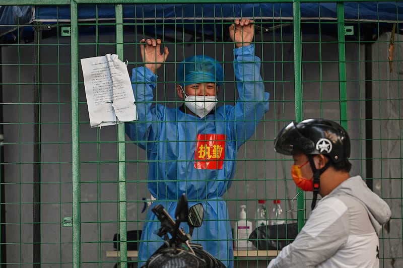 A worker wearing protective gear and standing behind a fence in a residential area under COVID-19 lockdown talks with a man on a scooter in the Xuhui district of Shanghai on June 16, 2022.