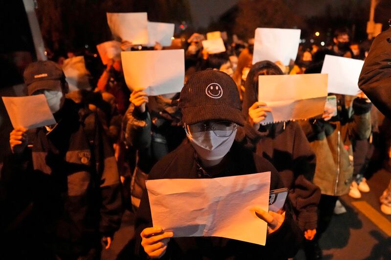 Protesters hold up blank pieces of paper and chant slogans as they march to protest strict COVID-19 measures in Beijing, Nov. 27, 2022. (Ng Han Guan/AP)