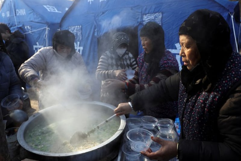 A woman distributes food at a temporary shelter for earthquake victims at Yangwa village, following the earthquake in northwestern China's Gansu province, Dec. 21, 2023. (Xiaoyu Yin/Reuters)