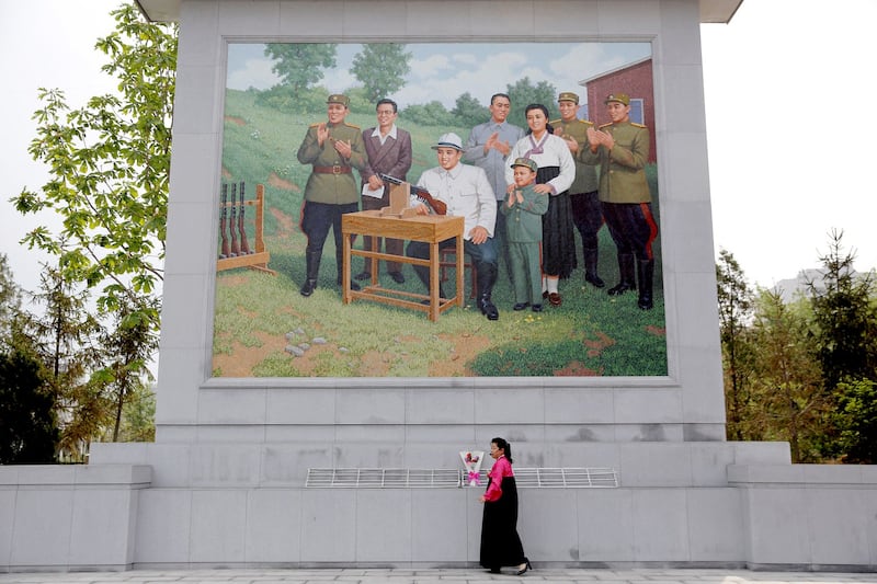 A guide adjusts flowers under a mural showing former North Korean leader Kim Il Sung (seated); his son and successor Kim Jong Il as a child, and his first wife Kim Jong Suk, at the former ammunition factory visited by foreign reporters on a government organized tour in central Pyongyang, North Korea May 5, 2016.