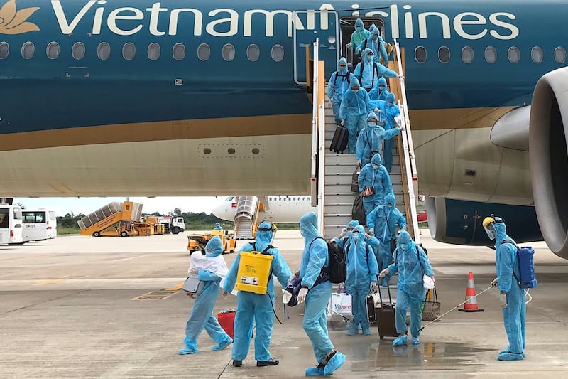 Healthcare workers spray disinfectant on Vietnamese nationals after their repatriation flight from Singapore landed at Can Tho airport, Vietnam, Aug. 7, 2020. Credit: Mai Nguyen/Reuters