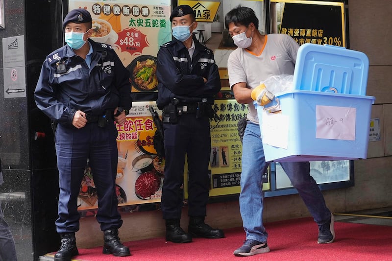 A worker carries containers past police officers during a raid on the office of Stand News in Hong Kong, Dec. 29, 2021. (Vincent Yu/AP)