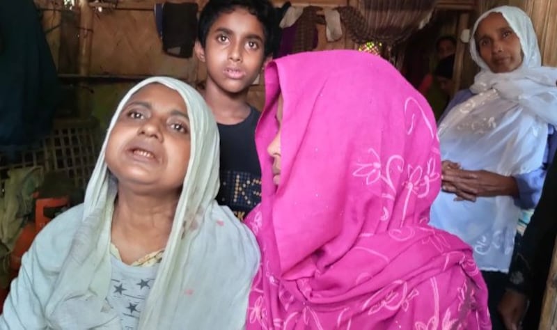 Sajeda Begum (left), the mother of slain Rohingya Azizul Haque, speaks to BenarNews in her shelter at the Balukhali camp in Ukhia, Bangladesh, as her other son, Noor Kodor, 12, who survived the same attack by gunmen, looks on, Oct. 22, 2021. Credit BenarNews