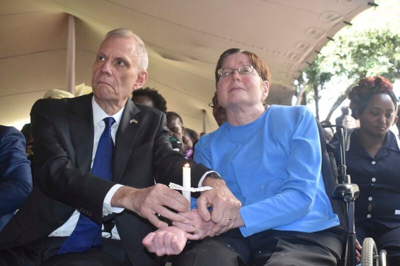 Then-U.S. Ambassador to Kenya Robert Godec (left) helps his wife, Lorri Godec Magnusson, hold a candle during the 20th commemoration of the 1998 bombing of the U.S Embassy in Nairobi, Aug. 7, 2018. Mrs. Godec was left paralyzed and confined to a wheelchair after the bombing. Credit: AP