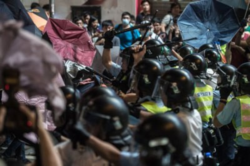 Police use batons to hit pro-democracy protesters (L) using raised umbrellas for protection during a clash in the Mongkok district of Hong Kong, Oct. 17, 2014. Credit: AFP