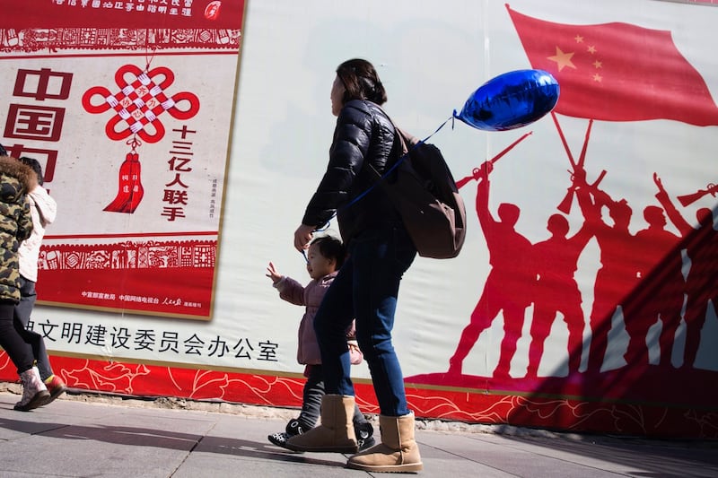 2016 年 3 月 8 日，星期二，中国北京街头，一名孩子走在政府宣传标语附近，标语“13 亿人团结”一名卫生官员周二表示，允许所有夫妇生两个孩子而不是一个孩子。（美联社）