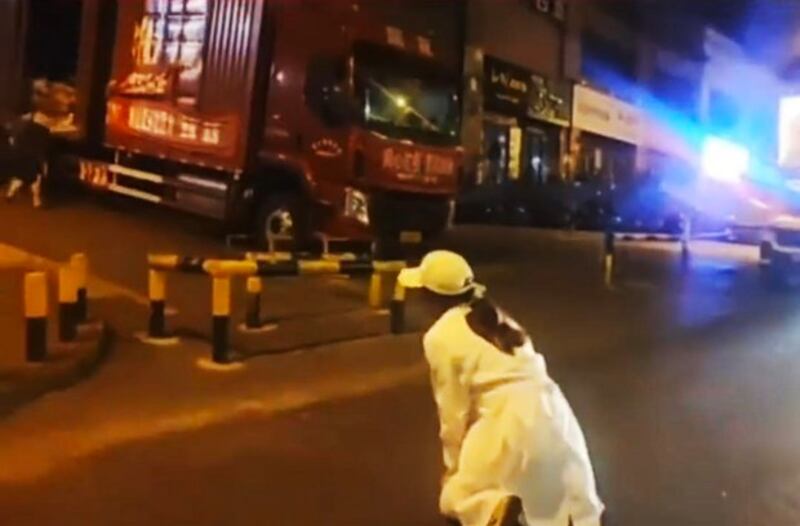 In a screenshot of a video labeled as being shot in Guiyang and posted to social media, a middle-aged woman kneels in the middle of the street asking for food from people unloading goods. Credit: citizen journalist