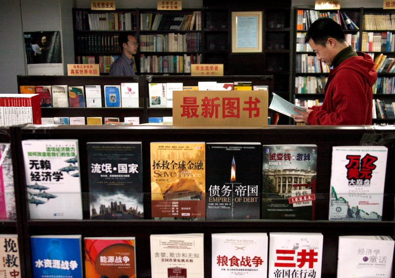 A Chinese man reads a book as another walks between shelves at the 'Utopia' bookshop in central Beijing in this March 25, 2009 file picture.