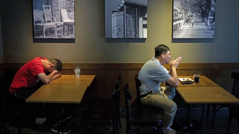 A Chinese man (L) takes a nap while another man talks on his smartphone using headphones inside a coffee shop in Beijing, Aug. 28, 2018.