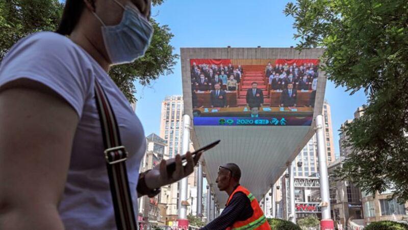 A woman wearing a protective face mask walks near an outdoor screen of a news report about Chinese President Xi Jinping attending the closing ceremony of the National People's Congress in Beijing, May 28, 2020.