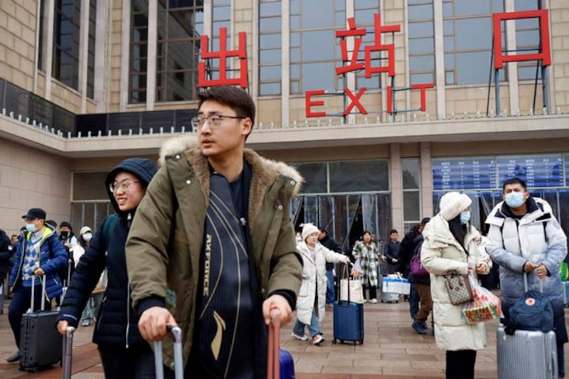 Travelers walk with their luggage outside the Beijing railway station in Beijing, China, Feb. 18, 2024. (Florence Lo/Reuters)