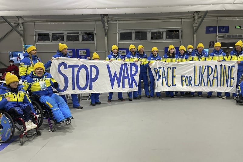 This handout photo taken and released on by the Ukraine delegation shows delegation members holding banners to call for peace prior to the opening ceremony of the Beijing 2022 Winter Paralympic Games at the National Stadium in Beijing, March 4, 2022. Credit: AFP