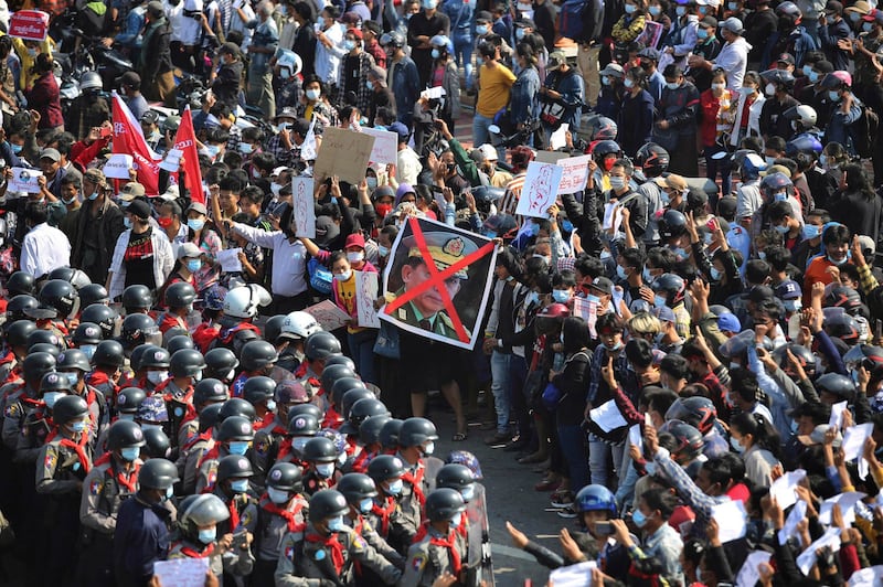 Protesters flashing three fingered salutes and displaying a defaced image of junta leader Min Aung Hlaing faceoff with a line of riot policemen in Naypyitaw, Myanmar, Feb. 8, 2021. Credit: AP