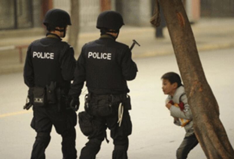 A Tibetan boy (R) looks on as armed Chinese police patrol a street in Chengdu in Sichuan province, Jan. 27, 2012.