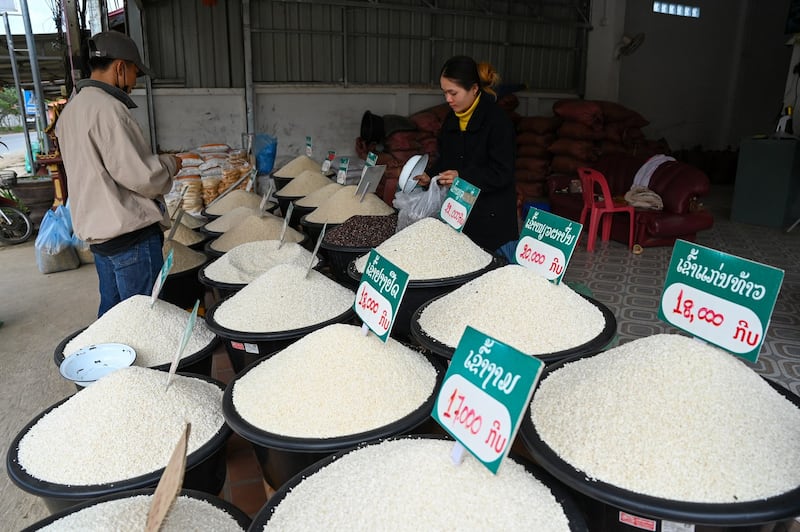 A vendor, right, fills rice in a plastic bag for her customer, January 27, 2024, in Luang Prabang, Laos. (Tang Chhin Sothy/AFP)