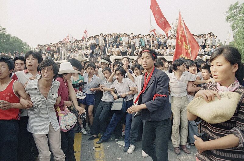 1989年6月3日，在北京人民大会堂附近，支持民主的抗议者手挽手阻止愤怒的人群追逐撤退的士兵。（美联社）