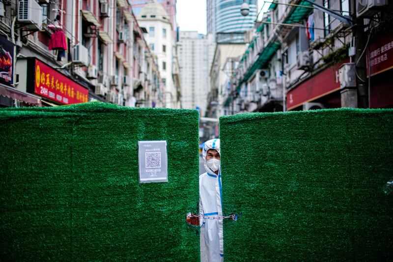 A worker in a protective suit looks out through a gap in barriers at a closed residential area during lockdown, amid the coronavirus disease (COVID-19) pandemic, in Shanghai, China, May 25, 2022. Credit: Reuters.